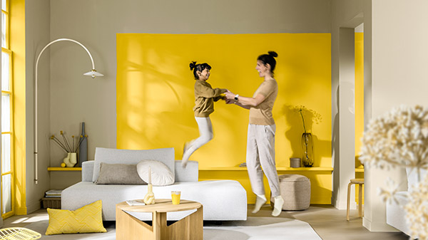 A parent and child jumping in a modern living room. Behind them is a statement feature wall painted in yellow. 